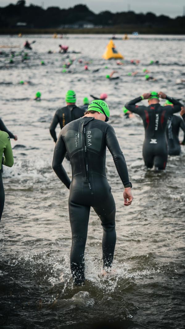 Swimmers in wetsuits wading out of the water